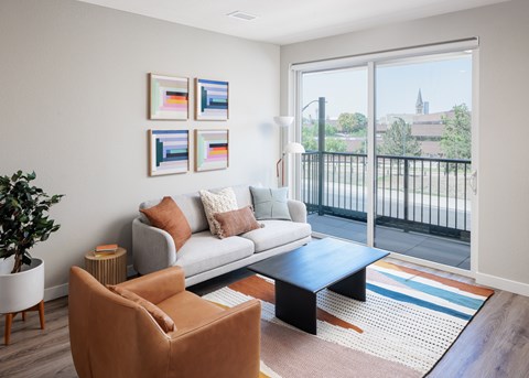 A living room with a grey couch, a brown chair, a coffee table and a plant.