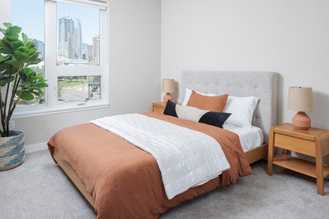 A bedroom with a large bed and a city view through the window.