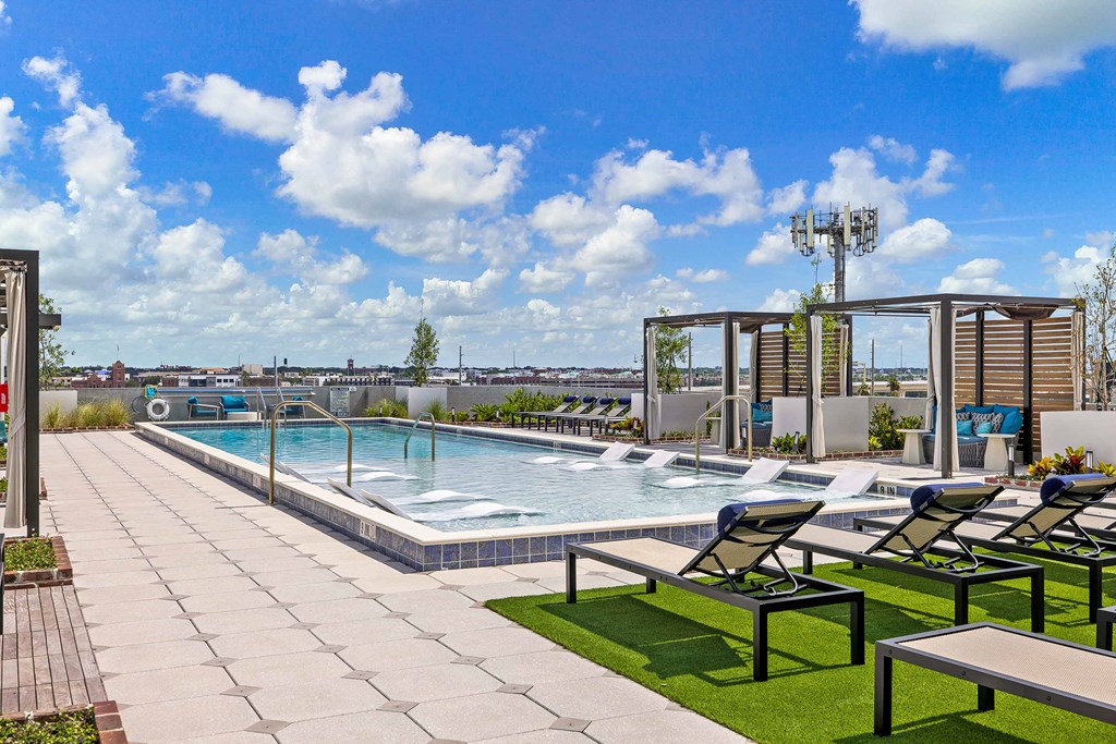 a swimming pool on the rooftop of a building with lounge chairs and tables