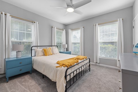 A bedroom with a bed, dresser, and window with blinds.