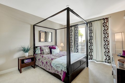 A bedroom with a four poster bed and a window with curtains.