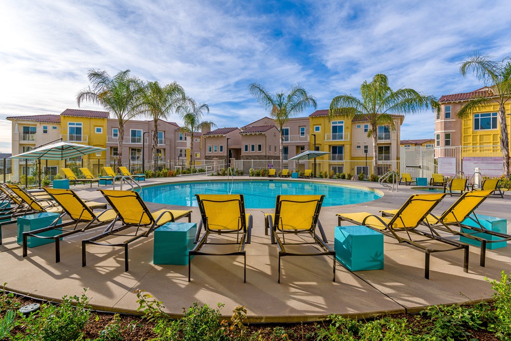 A pool surrounded by yellow chairs and palm trees.