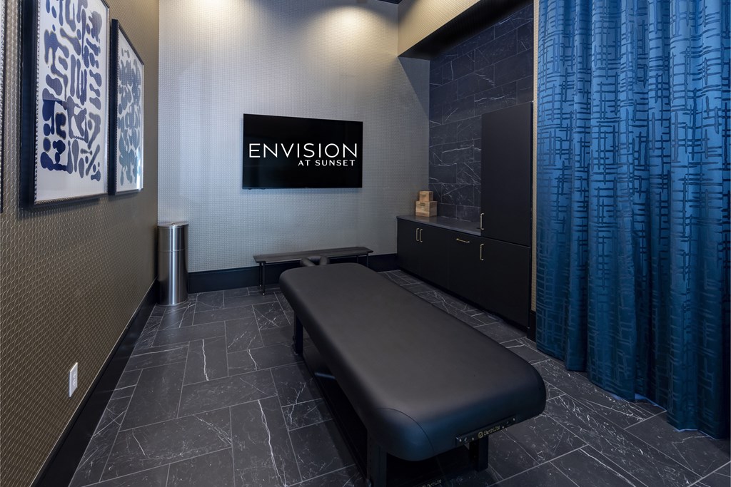 A black massage table in a room with a blue curtain.