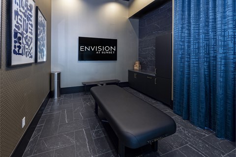 A black massage table in a room with a blue curtain.