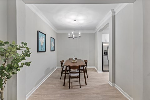 A dining room with a table set for two and a plant on the left.