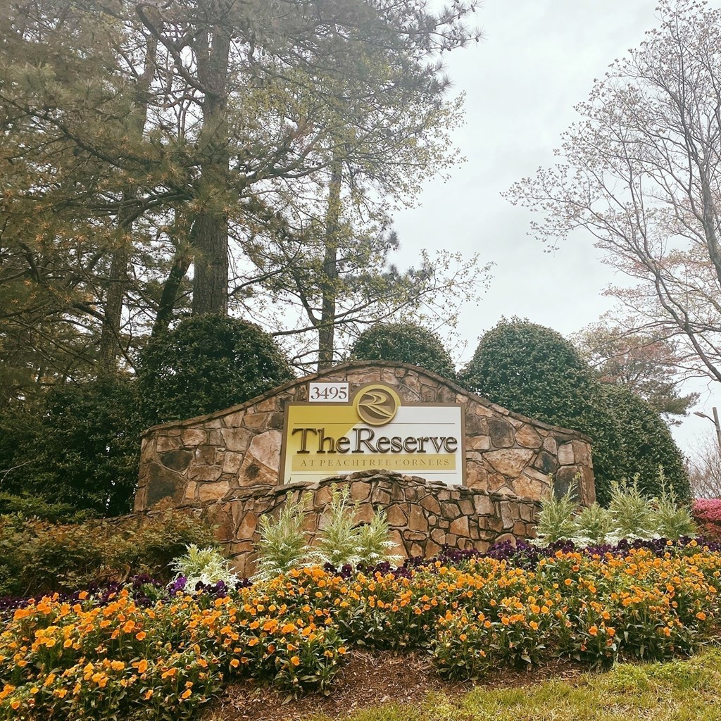 A sign for The Reserve surrounded by flowers and trees.