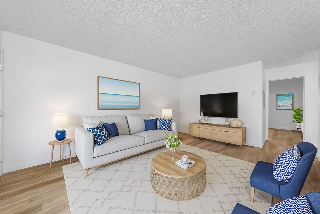 A living room with a white couch, blue chairs, and a painting on the wall.