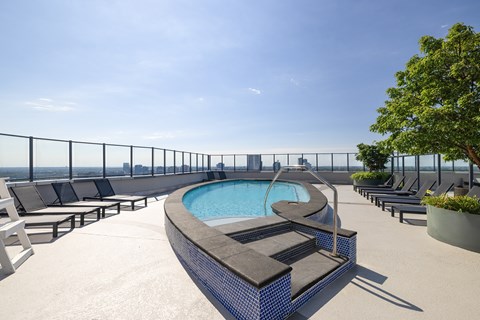 A pool on a rooftop with lounge chairs and a fence.