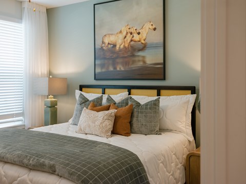 A bedroom with a bed, pillows, a lamp, and a painting of a horse.