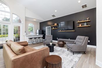 A living room with a brown couch, a grey armchair, and a black wall.