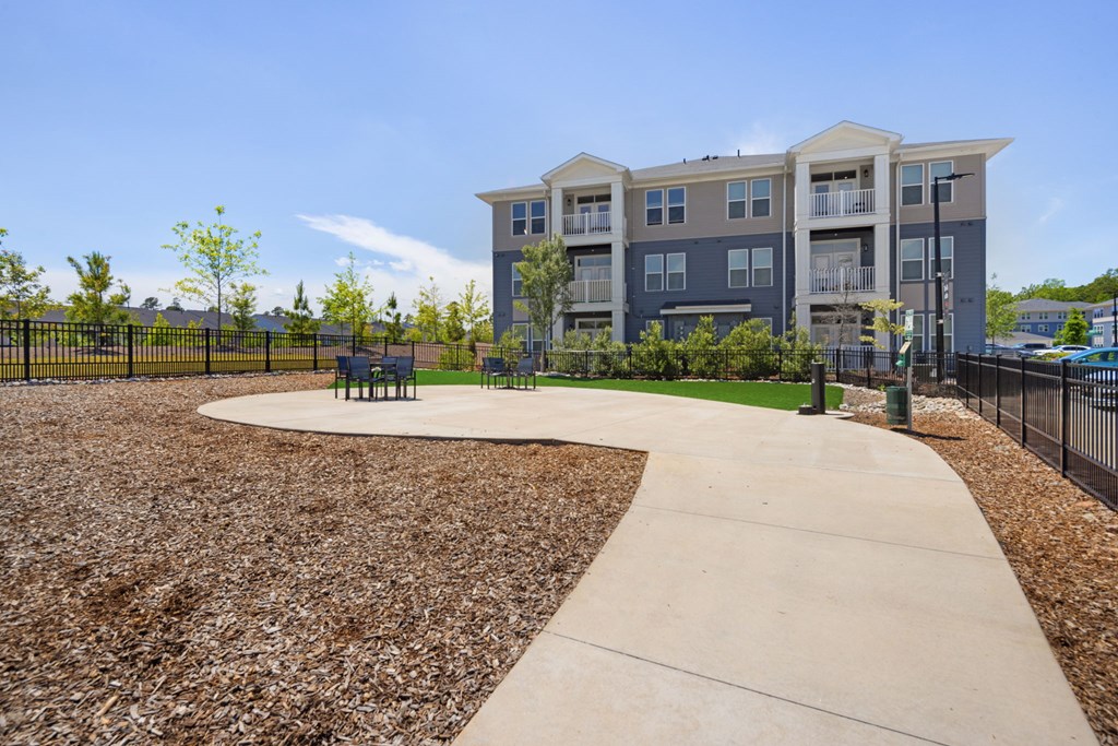 A concrete walkway leads to a building with a fenced in yard.