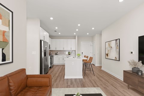 A modern living room with a brown leather couch and a kitchen in the background.