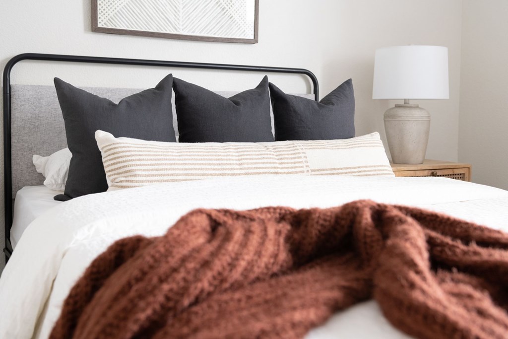 A bed with a white comforter and a brown blanket.