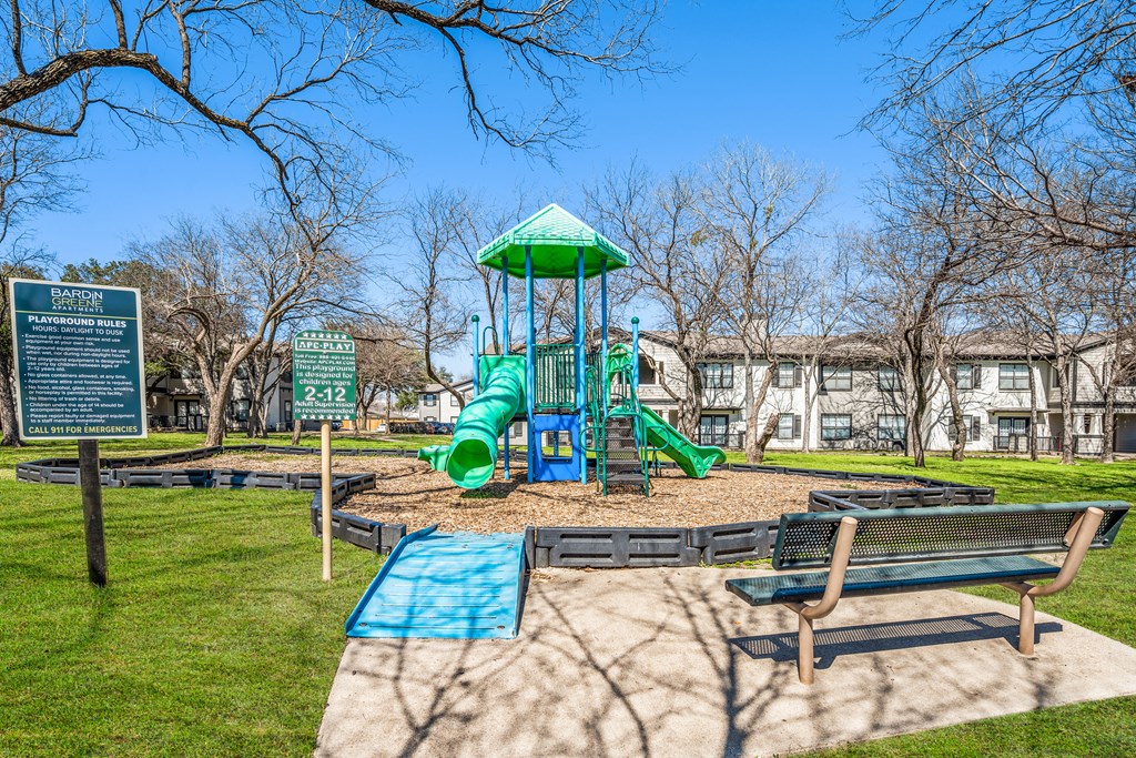 a playground with a green slide and benches in a park