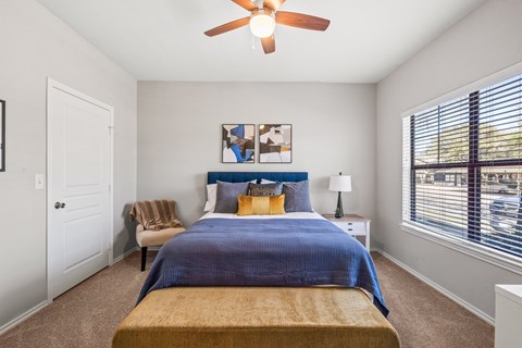 A bedroom with a bed, a ceiling fan, and a large window at Bardin Greene apartments in Arlington, Texas.