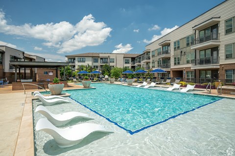 A large swimming pool surrounded by white lounge chairs and umbrellas.
