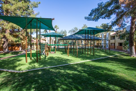 A playground with a green canopy and a white rope fence.