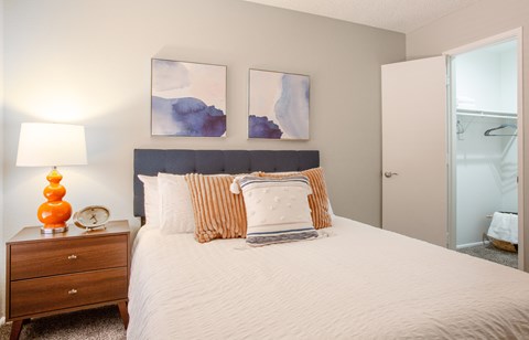 A bedroom with a bed, nightstand, and two paintings on the wall.