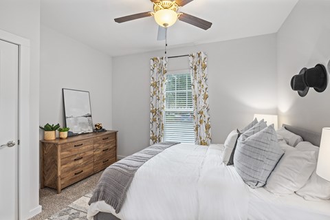 A bedroom with a bed, dresser, and window with curtains.