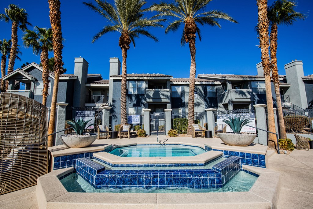 A pool surrounded by palm trees and a building in the background.