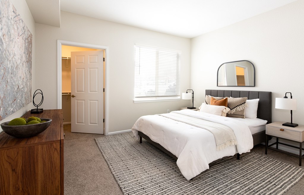 A bedroom with a large bed, a wooden dresser, and a bowl of fruit on the dresser.