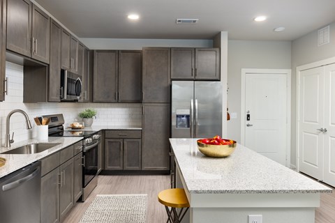 a kitchen with stainless steel appliances and a large island with a bowl of fruit