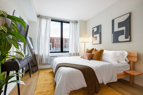 A bedroom with a large bed and a view of a cityscape through the window.