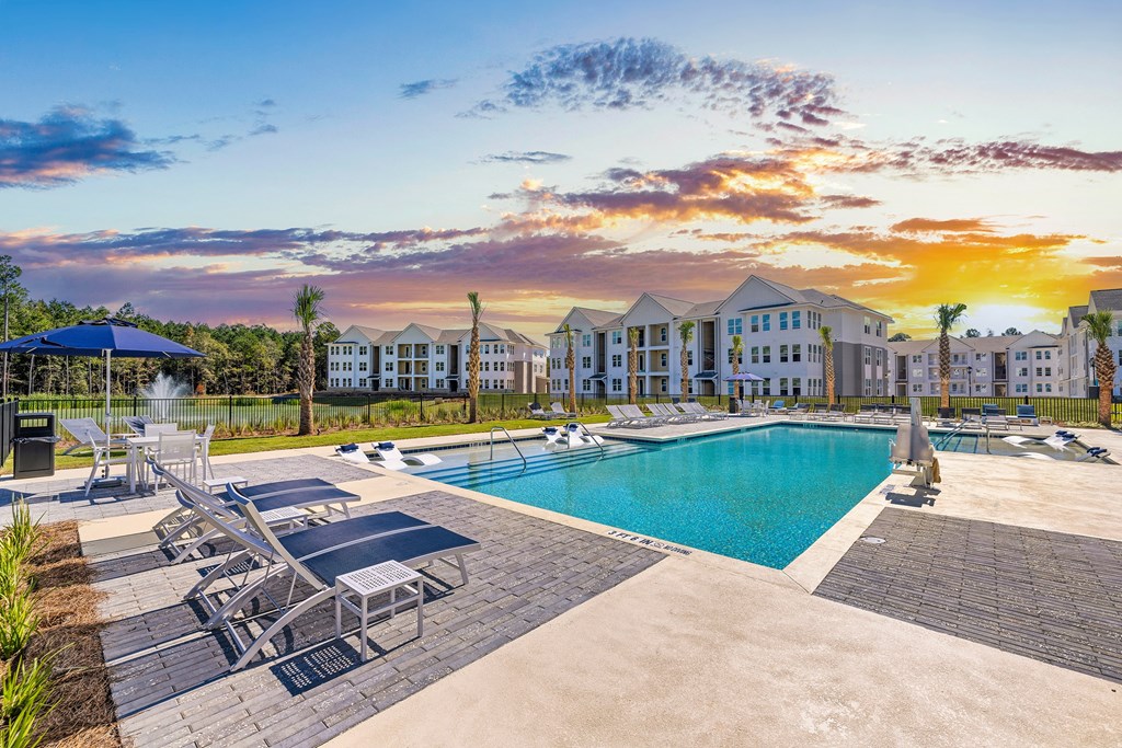 a swimming pool with chairs and umbrellas next to an apartment building