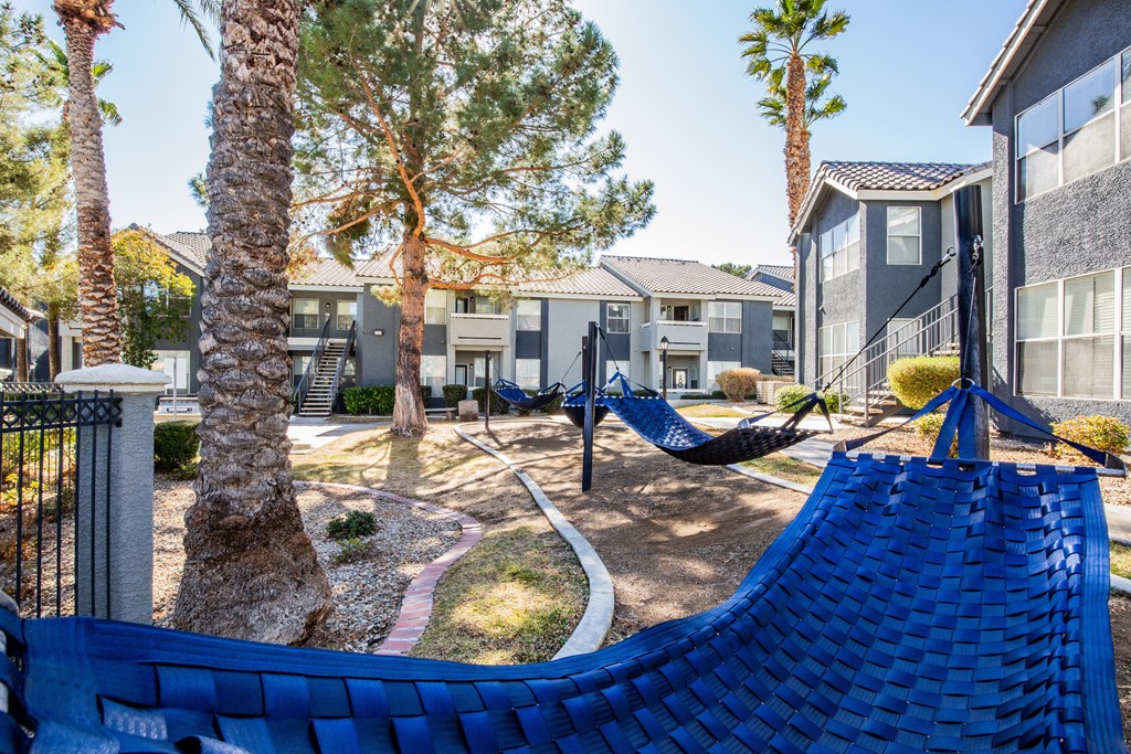 A blue hammock is in the foreground of a residential area with houses and palm trees.