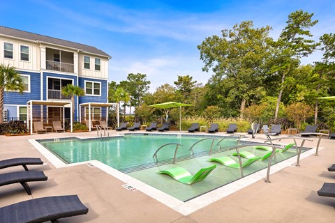 A large swimming pool with lounge chairs and a building in the background.