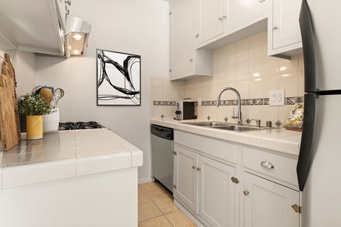 A white kitchen with a black fridge and a black and white picture on the wall.