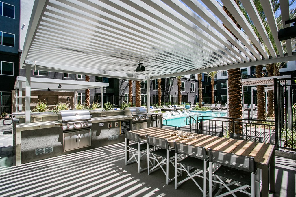 a patio with a long wooden table and chairs and a pool in the background