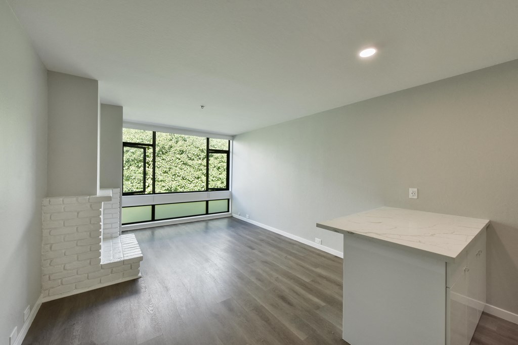 an empty living room with a kitchen and a window