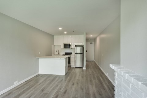 an empty living room with a kitchen with a stove and refrigerator