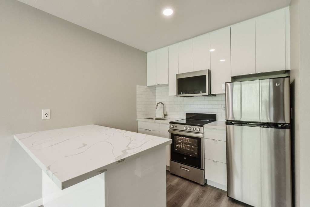 a white kitchen with stainless steel appliances and a marble counter top