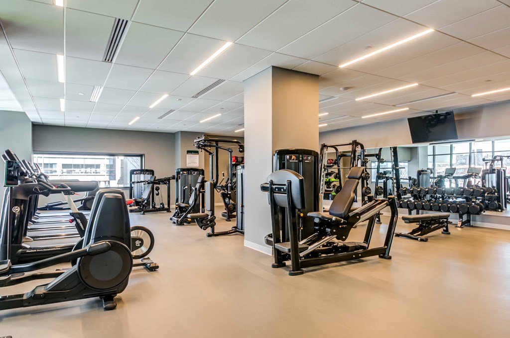a gym with cardio equipment and weights in a building with windows