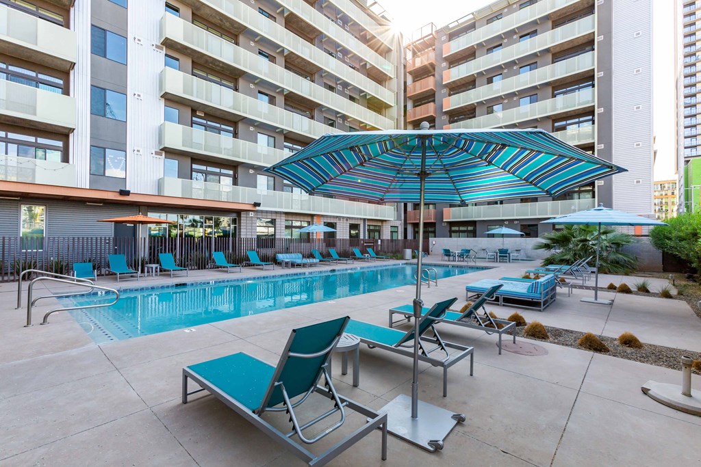 a swimming pool with lounge chairs and umbrellas in front of an apartment building