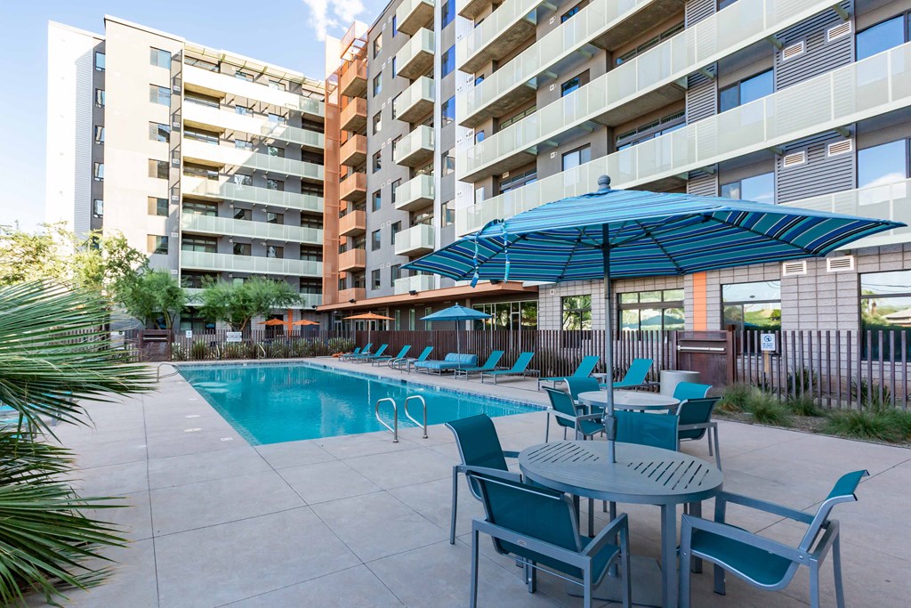 a swimming pool with chairs and umbrellas in front of an apartment building