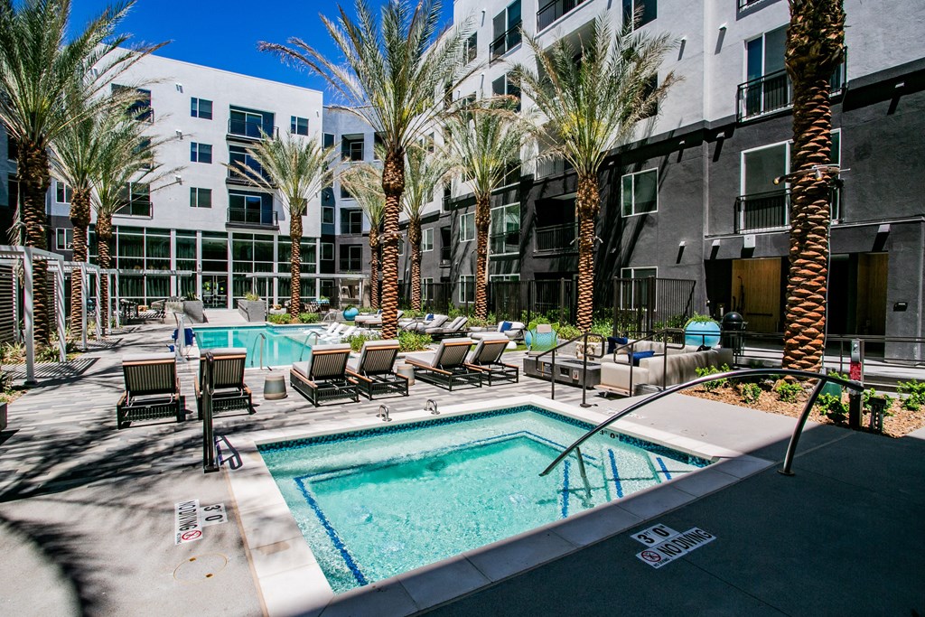 a pool with lounge chairs and palm trees in front of an apartment building