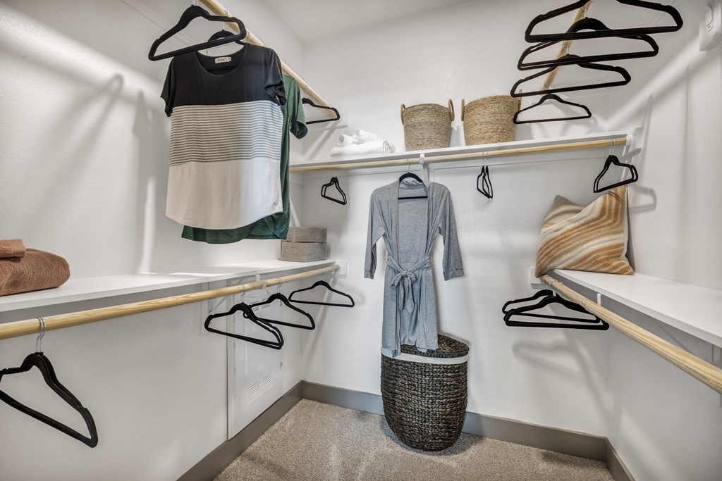 a walk in closet with white walls and shelves and clothes hanging on a rack