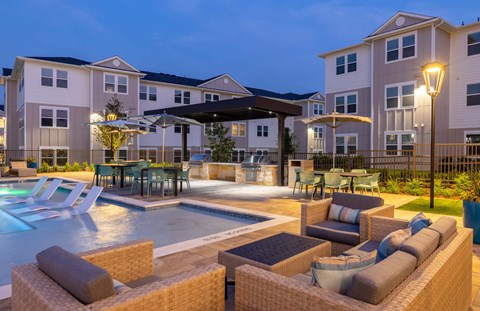a pool and patio area at night with apartments in the background