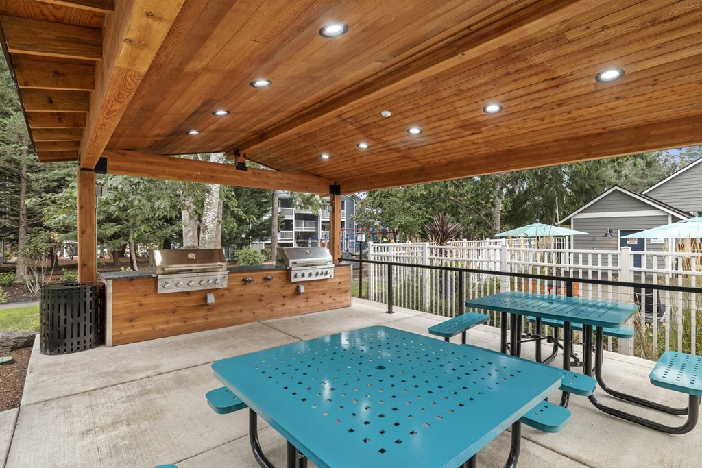 a covered patio with picnic tables and a barbecue grill