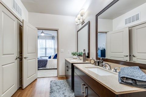 A bathroom with a vanity, mirror, and a bedroom in the background.