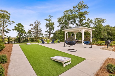 A white gazebo with blue chairs and a white bench sits in a grassy area.