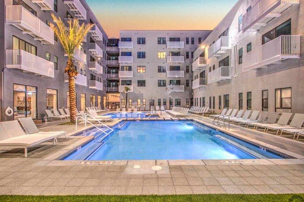a swimming pool with white lounge chairs and a palm tree in front of an apartment building