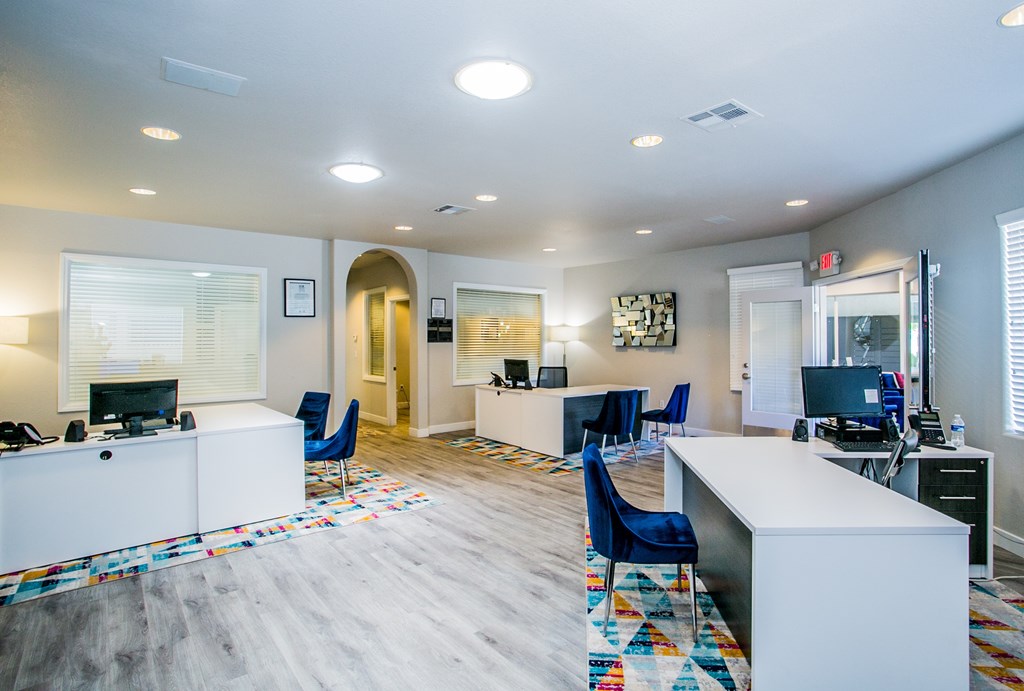 A spacious office with a white reception desk and blue chairs.