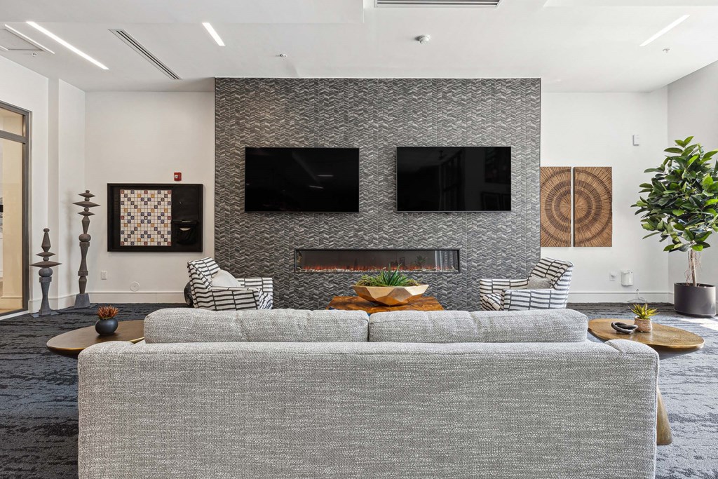 a living room with a gray couch and two televisions on the wall
