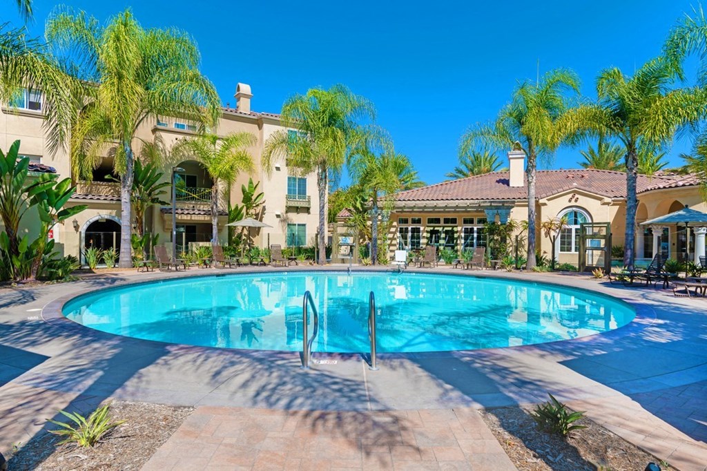 A large swimming pool surrounded by palm trees and a building in the background.