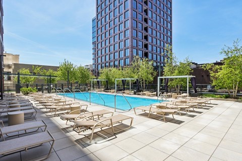 A pool surrounded by sun loungers and trees.