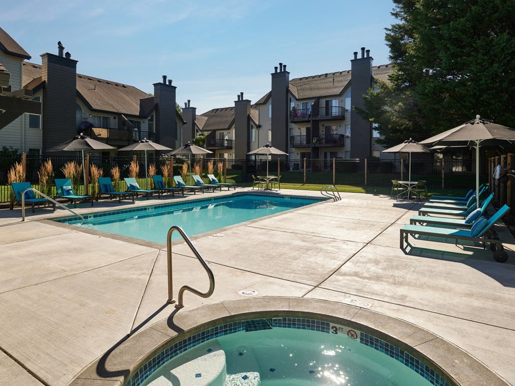 a swimming pool with blue chaise lounge chairs and umbrellas with apartment buildings in the